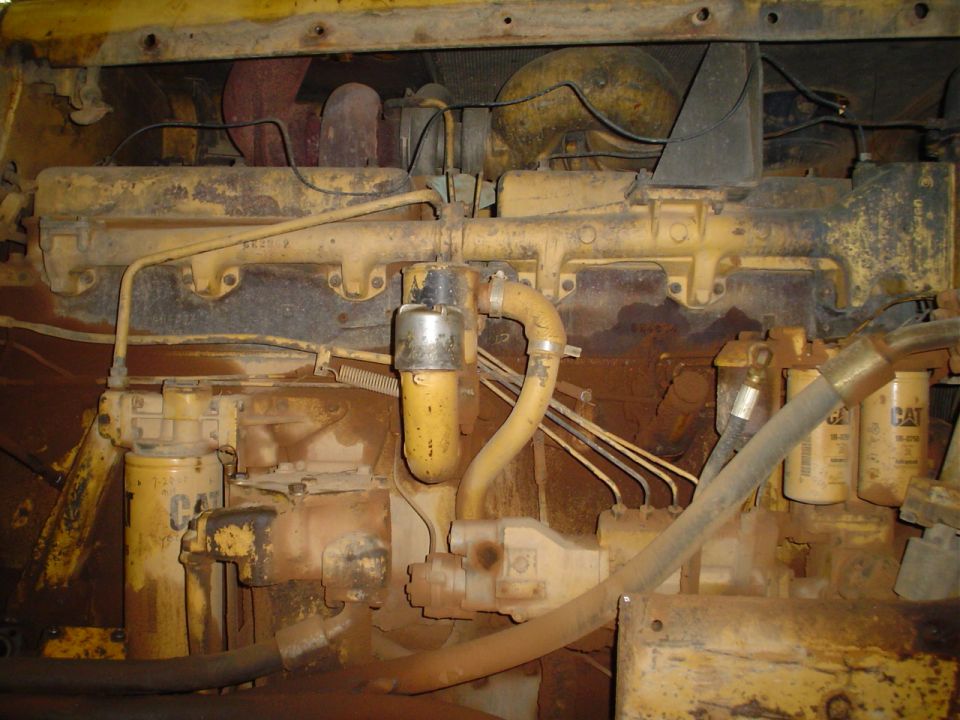 Yellow Caterpillar engine with oil filters and hoses, covered in dirt
