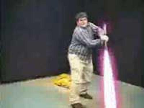 Person holding a pink toy lightsaber, standing in front of a dark background