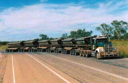 1990 Ford Bronco - long road train hauling several dump-style trailers on a rural two-lane highway under a blue sky with scattered clouds.