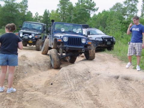 2002 Jeep Wrangler - A blue 2002 Jeep Wrangler navigates a sandy trail with other vehicles and people present.