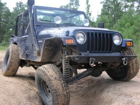 2002 Jeep Wrangler - This dark blue Jeep Wrangler, modified for off-road use with a snorkel and large tires, navigates a dirt track.