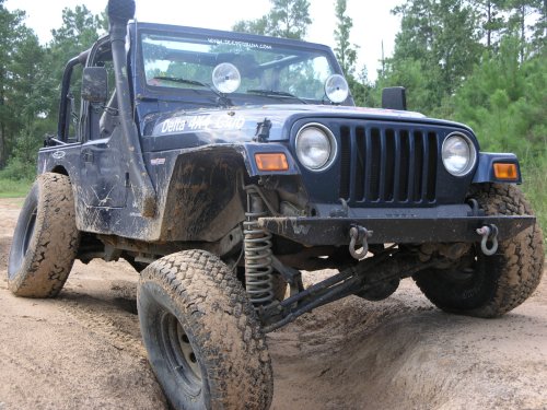 Muddy dark blue lifted Jeep Wrangler on off-road tires on sandy terrain