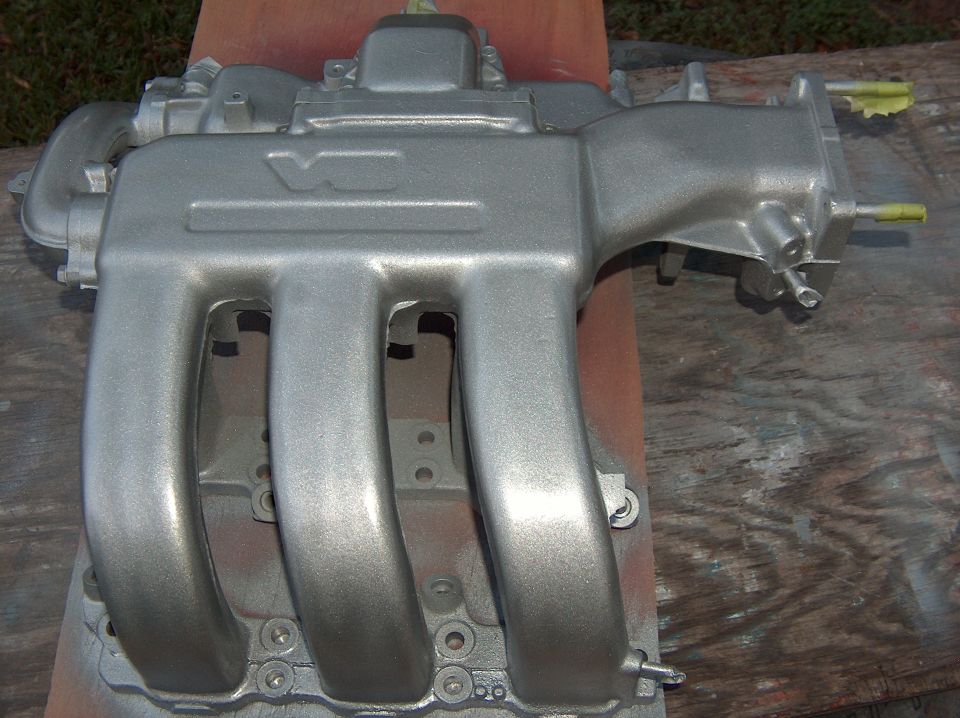 Silver-painted V6 intake manifold with curved runners on wood planks