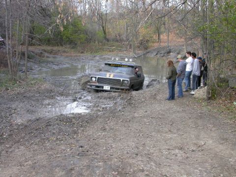 Front view of a dark 1978 Ford Bronco stuck in mud, with spectators watching