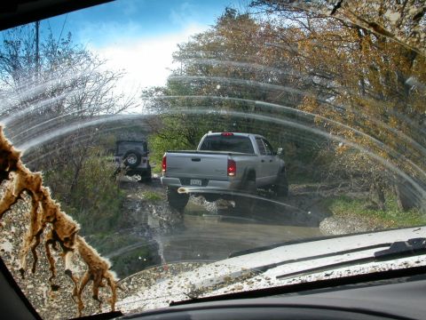 1996 Ford Bronco — Silver pickup truck and black Jeep driving on a muddy trail
