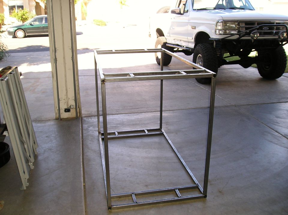Welded square-tube steel frame on a driveway with a white lifted Ford truck behind