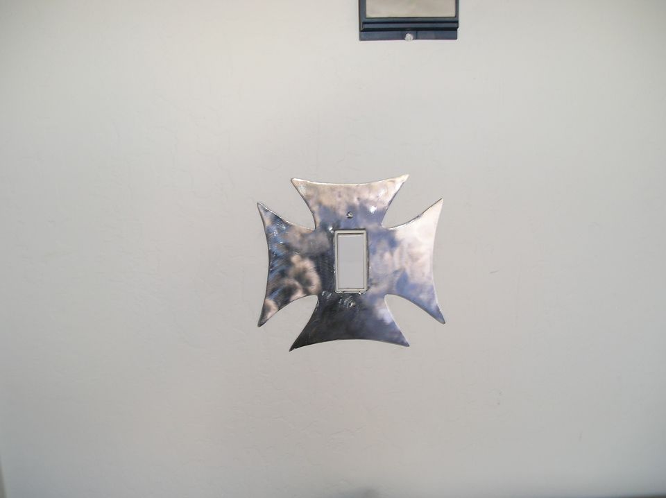 Polished Maltese cross switch plate around a white rocker switch on a white wall