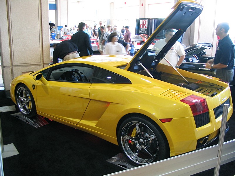 Yellow sports car with rear engine compartment open, showing some components. Chrome wheels and red brake calipers are visible