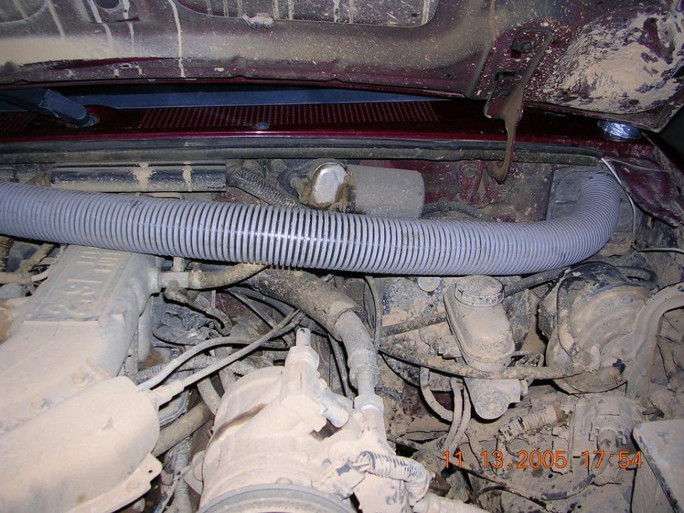 Gray corrugated flexible hose routed across a dusty engine bay with maroon body panels.