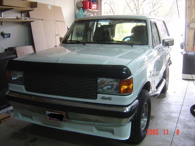 White Ford Bronco with billet grille and hood deflector parked in a garage, front three-quarter view