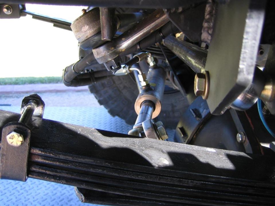 Underside of a lifted truck's front leaf spring, tie rod and steering stabilizer