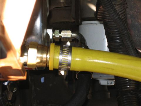 1994 Ford Bronco - Close-up view of a yellow hose connected with metal fittings and a hose clamp, with visible text 'SUPERMOTORS' at the bottom right.