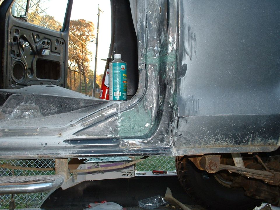Close-up of stripped door sill and rocker area on a dark Bronco during bodywork, door open, tools and supplies nearby