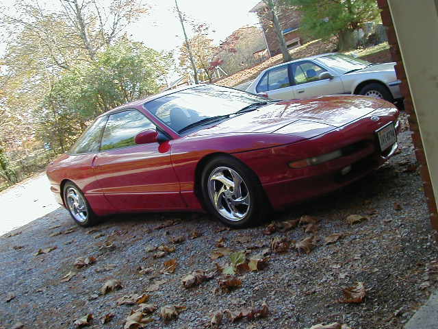 Red 1994 Ford Probe parked on gravel with a silver sedan behind it
