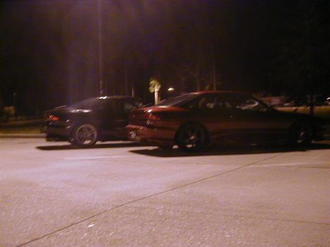 1994 Ford Probe - Two cars, a red 1994 Ford Probe and a black car, are parked next to each other in a lot at night.