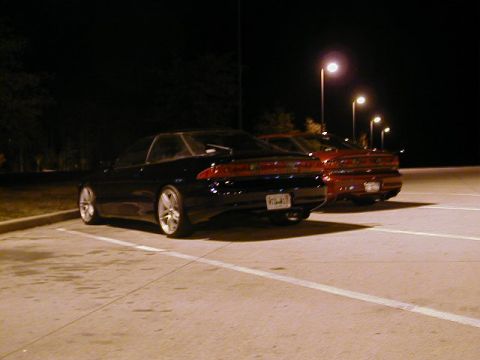 1994 Ford Probe - Two coupes are parked in a lot at night, illuminated by streetlights.