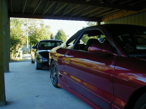 1994 Ford Probe - Two Ford Probes are parked side-by-side under a carport, with trees and foliage visible in the background.