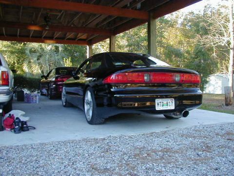 1994 Ford Probe - A black sports car with a license plate MTD 817 is parked under a covered area next to another vehicle.