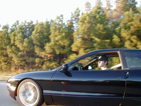 1994 Ford Probe - A black coupe drives down a road with trees in the background.