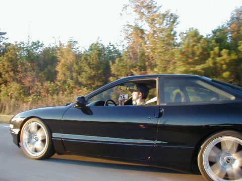 1994 Ford Probe - A black 1994 Ford Probe is captured in a side profile shot while driving, with a driver holding a camera.