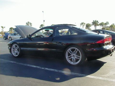1994 Ford Probe - A black coupe with its hood up and aftermarket wheels is parked in a lot with other vehicles.