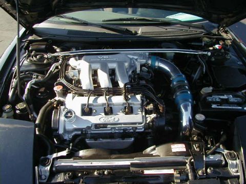 1994 Ford Probe - The engine bay of a car, a V6 engine with custom blue intake piping and a strut bar.