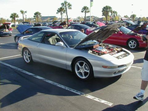 1994 Ford Probe - Several cars are parked in a lot, with one silver coupe's hood open to reveal the engine.