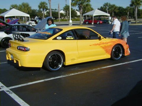 1994 Ford Probe - A yellow 1994 Ford Probe with custom flame graphics and a large rear spoiler is displayed at an outdoor event.