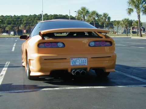 1994 Ford Probe - This orange sports coupe is parked in a lot, showing off its custom body kit and quad exhaust pipes.