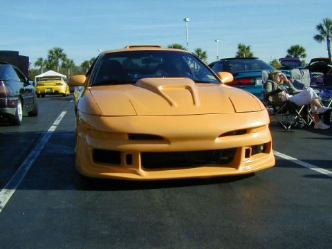 1994 Ford Probe - A yellow car with a custom hood scoop is parked in a lot, with other vehicles and people visible in the background.