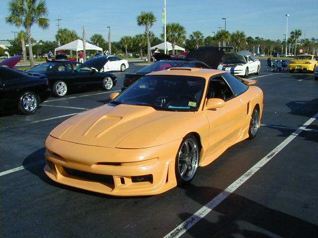 Orange 1994 Ford Probe with custom body kit and aftermarket wheels parked in a lot with other cars