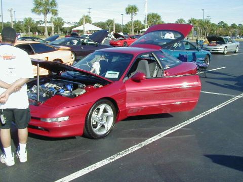 1994 Ford Probe - Several cars are displayed with hoods and doors open at an outdoor car show.