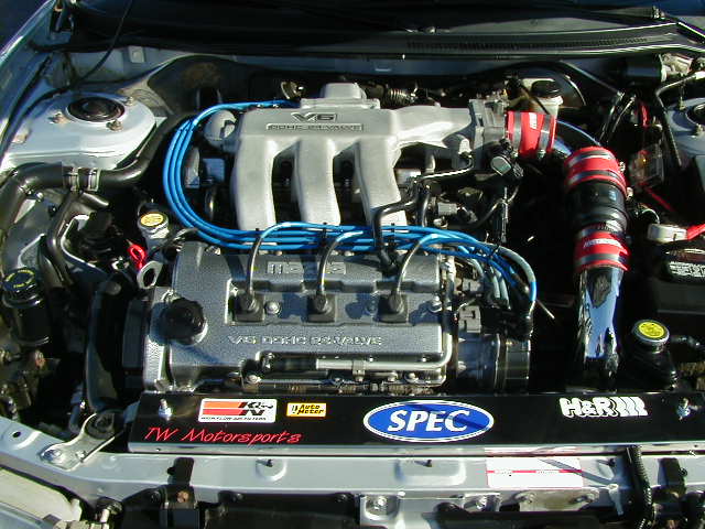 Engine bay with V6 DOHC engine, blue spark plug wires, and aftermarket parts. Silver car