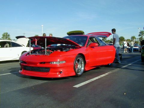 1994 Ford Probe - A red 1994 Ford Probe is displayed with its hood and door open at an outdoor car show.