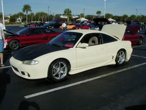 1994 Ford Probe - A modified coupe with a black hood and custom body kit is parked at an outdoor car show.
