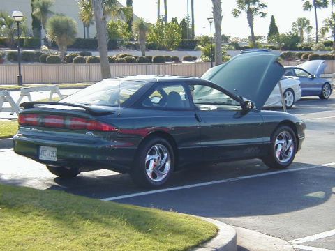 1994 Ford Probe - A dark green 1994 Ford Probe coupe is parked in a lot, with other vehicles visible in the background.