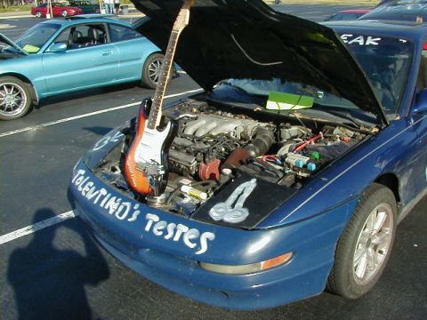 1994 Ford Probe - A blue car's engine bay is displayed with a guitar inside, accompanied by custom text and drawings on the car's body.