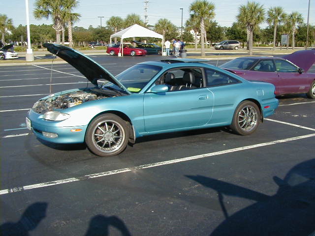 Blue coupe with hood open, parked in a lot. Chrome wheels visible