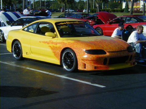 1994 Ford Probe - A yellow sports car with custom flame graphics is parked at an outdoor event.