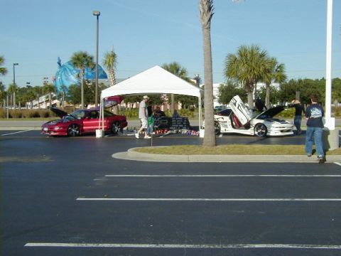 1994 Ford Probe - Two cars are displayed under a tent at an outdoor event, with people milling around.