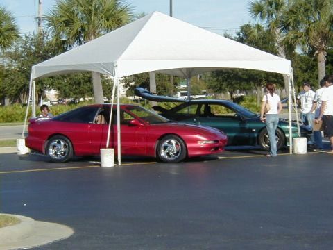 1994 Ford Probe - Two cars, a red sports car and a green sedan, are parked under a white tent at an outdoor event.