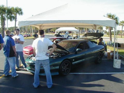 1994 Ford Probe - A group of people stand around a green 1994 Ford Probe with its hood open at an outdoor event.