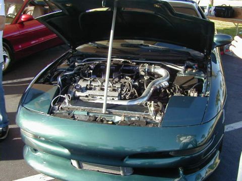 1994 Ford Probe - The engine bay of a green car is displayed with the hood up. Another car is visible in the background.