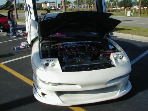 1994 Ford Probe - A white coupe with custom butterfly doors and hood open, revealing the engine bay. The car features PIAA lighting components.