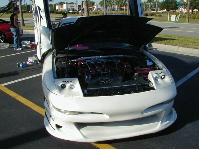 White coupe with butterfly doors and hood open, engine visible. PIAA lights