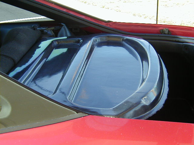 Close-up of a blue plastic speaker cover in the rear of a car. Red exterior paint is visible