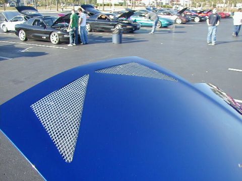 1994 Ford Probe - A blue car's hood with distinctive mesh vents is shown, with a car meet in the background.