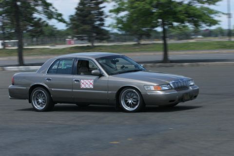 2001 Mercury Grand Marquis - A 2001 Mercury Grand Marquis sedan is captured in motion, aftermarket wheels and a prominent door decal.