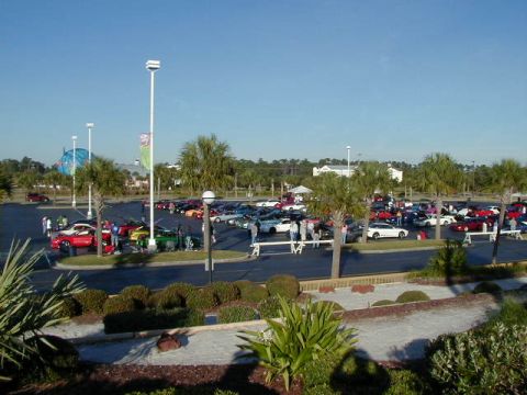 1994 Ford Probe - A large gathering of vehicles and people in a parking lot on a sunny day.