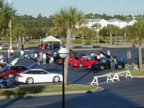 1994 Ford Probe - A collection of cars are gathered in a parking lot, with several people milling about.